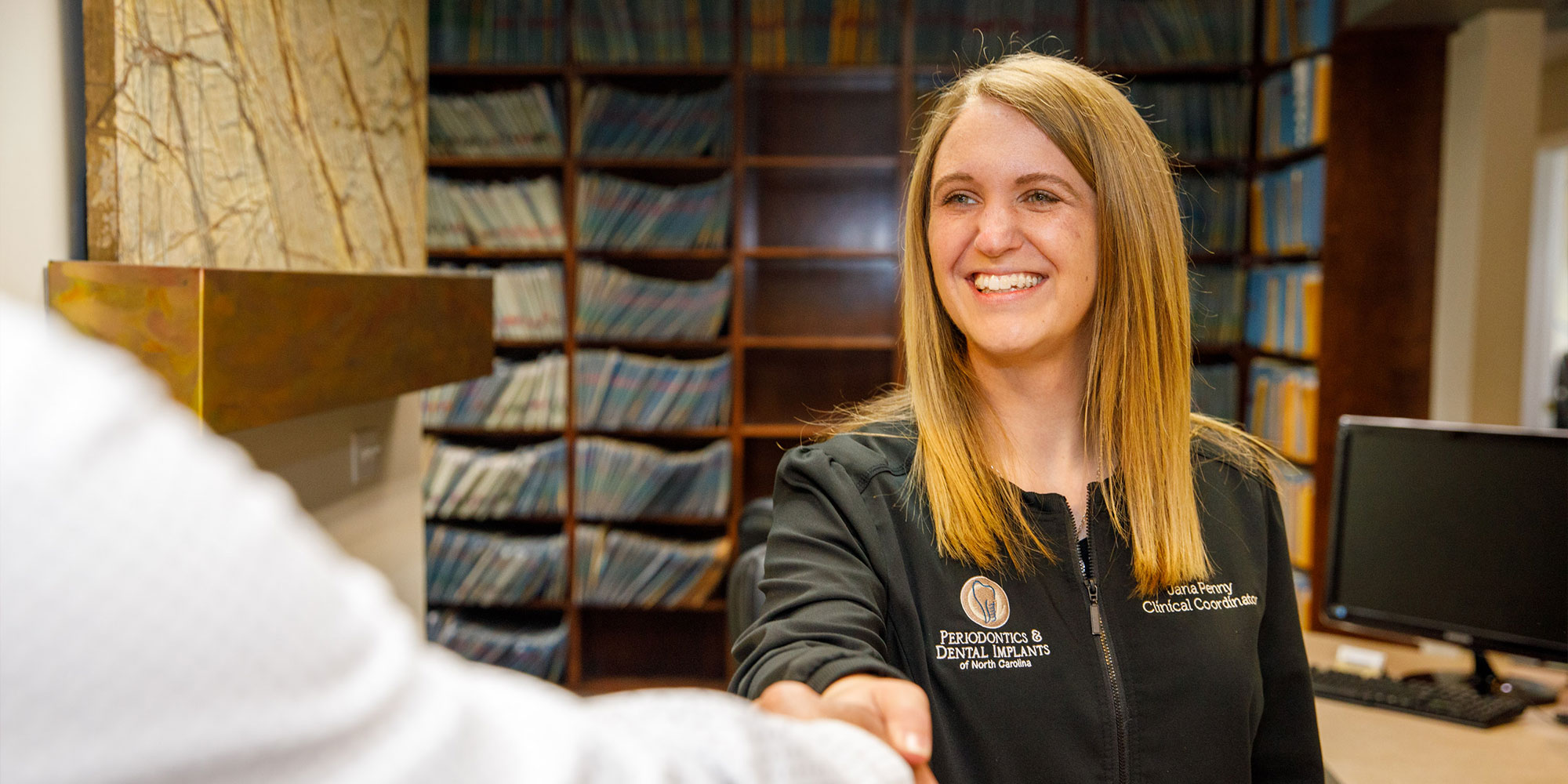 staff member shaking hands with patient at the front desk of the dental center
